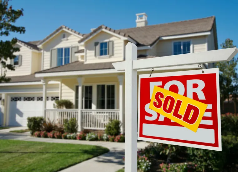 A ‘Sold’ banner across a For Sale sign in front of a two-storey suburban home